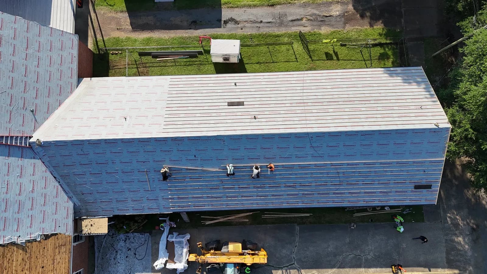 Aerial of a commercial roof tear-off in progress with crew laying new underlayment