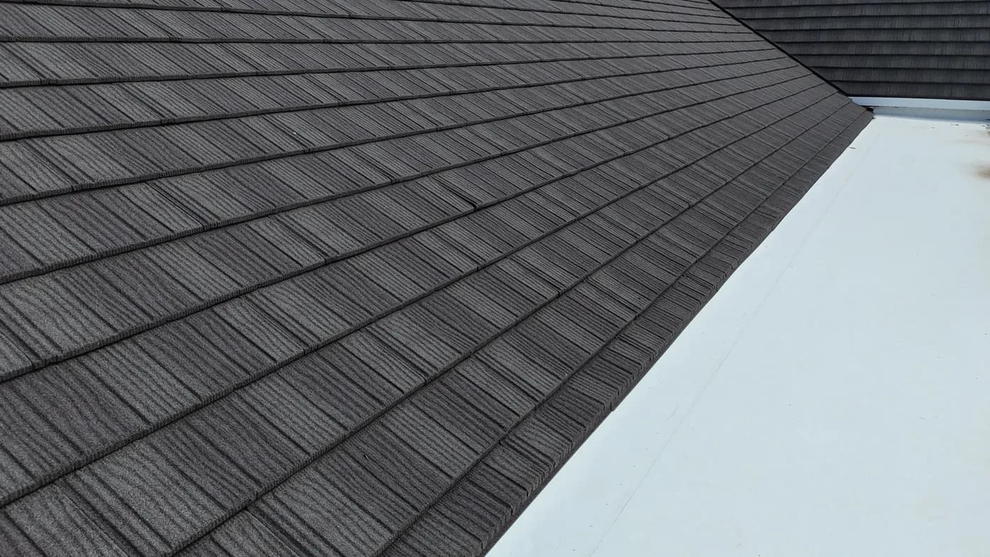 Close-up of stone-coated metal shingles meeting a white TPO low-slope section on a commercial roof