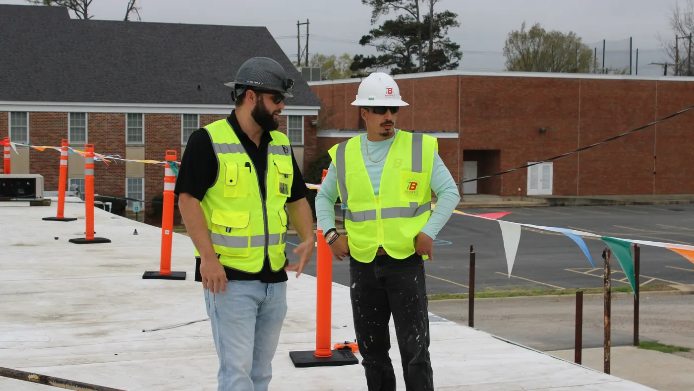 Two Brown's Roofing crew members in hi-vis safety vests on a commercial flat roof