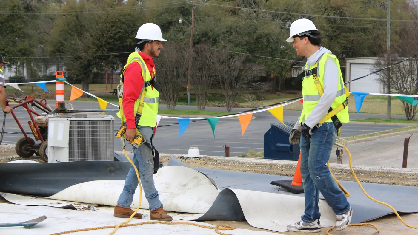 Two Brown's Roofing crew members in hard hats installing modified bitumen on a commercial flat roof