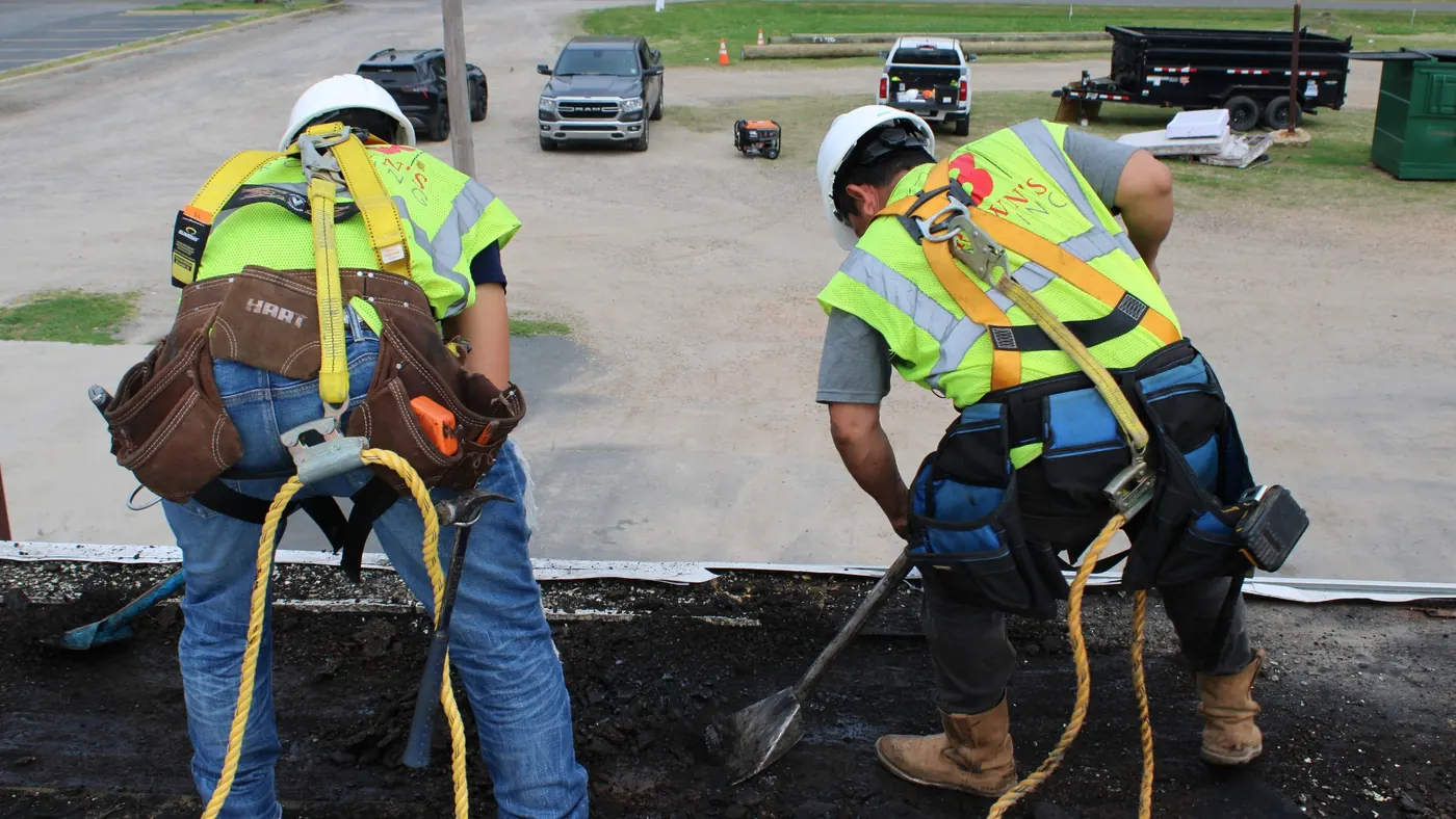 Brown's Roofing crew shoveling tear-off material at the edge of a commercial flat roof