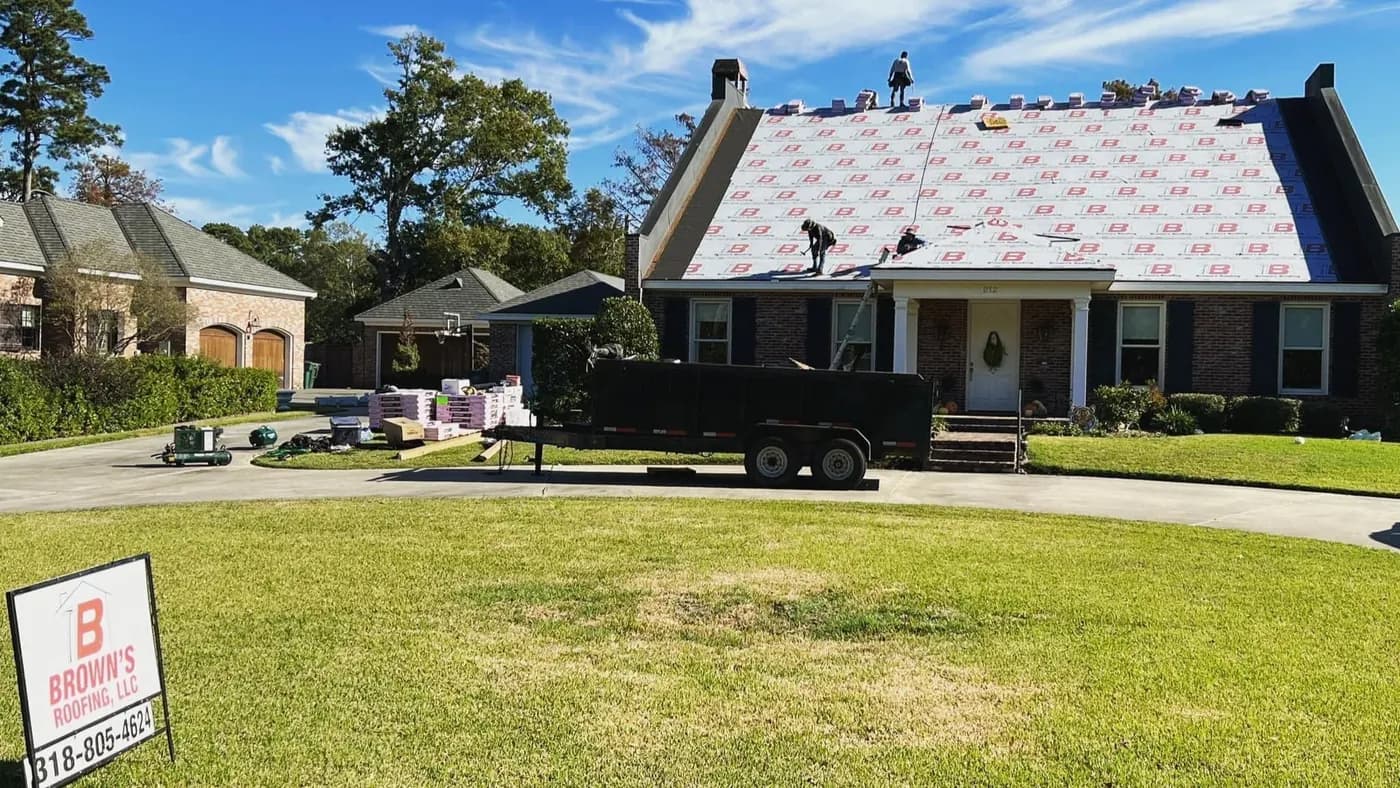 Brown's Roofing active job site: crew on a cottage roof laying red-pattern synthetic underlayment