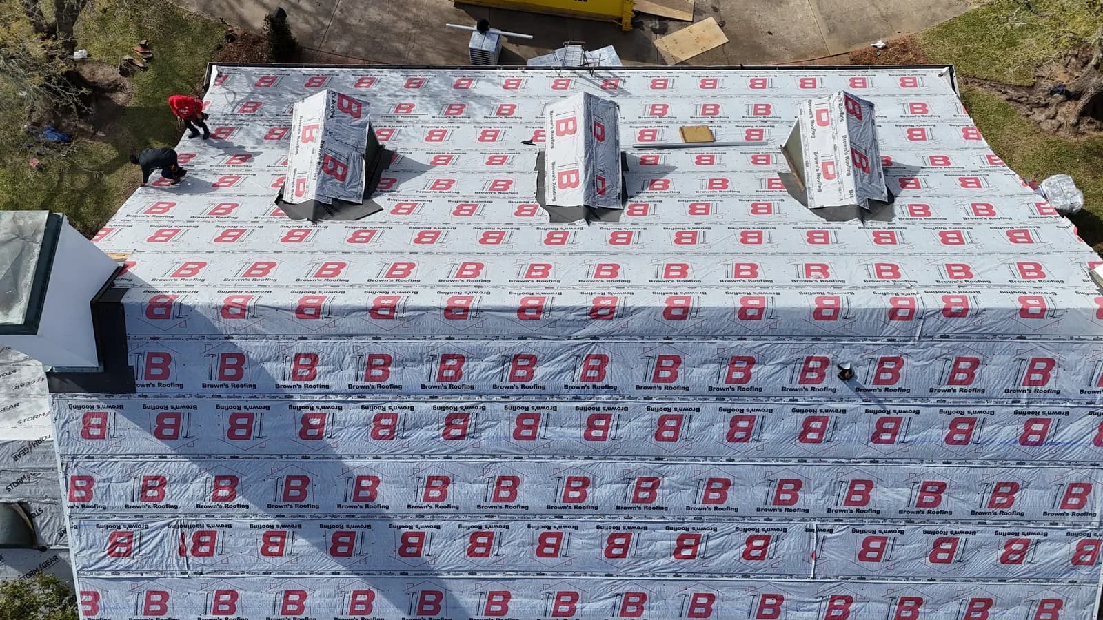 Aerial view of a residential reroof in progress with Brown's branded synthetic underlayment installed and shingle pallets staged on the roof
