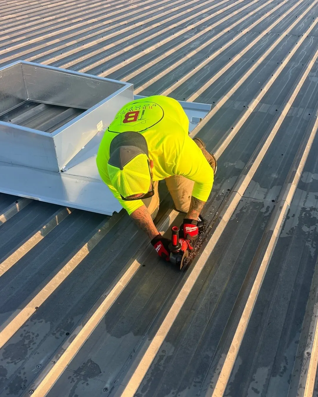Brown's Roofing crew member using a Milwaukee impact driver on a standing-seam metal roof