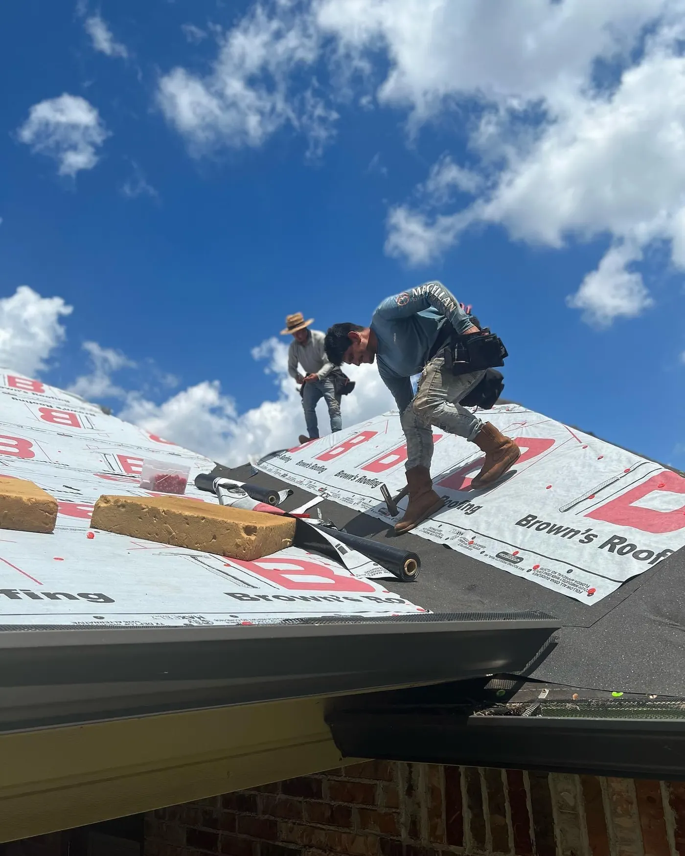 Brown's Roofing crew rolling out branded synthetic underlayment across a roof deck