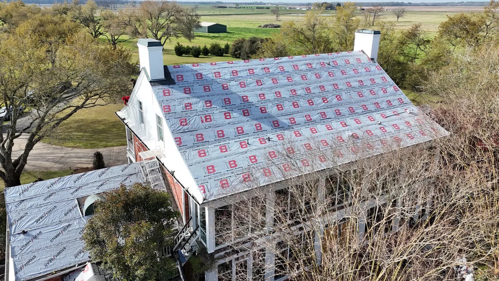 Aerial of a large two-story home mid-install with Brown's branded synthetic underlayment across the entire roof