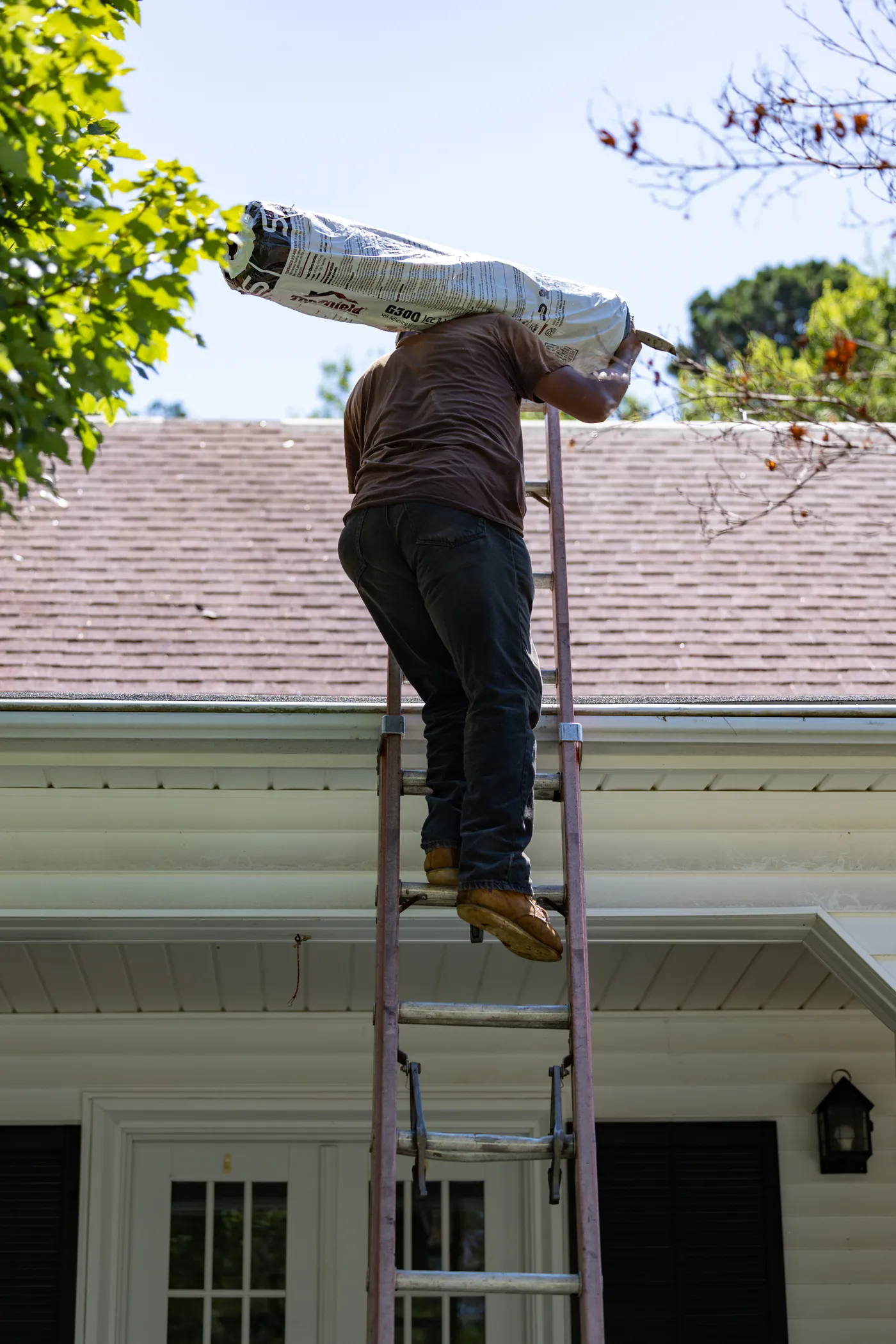 Brown's Roofing crew member climbing a ladder with a shingle bundle on his shoulder