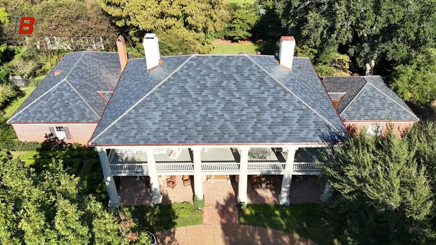 Drone aerial of a colonial brick home with wraparound columned porch and a new synthetic slate roof