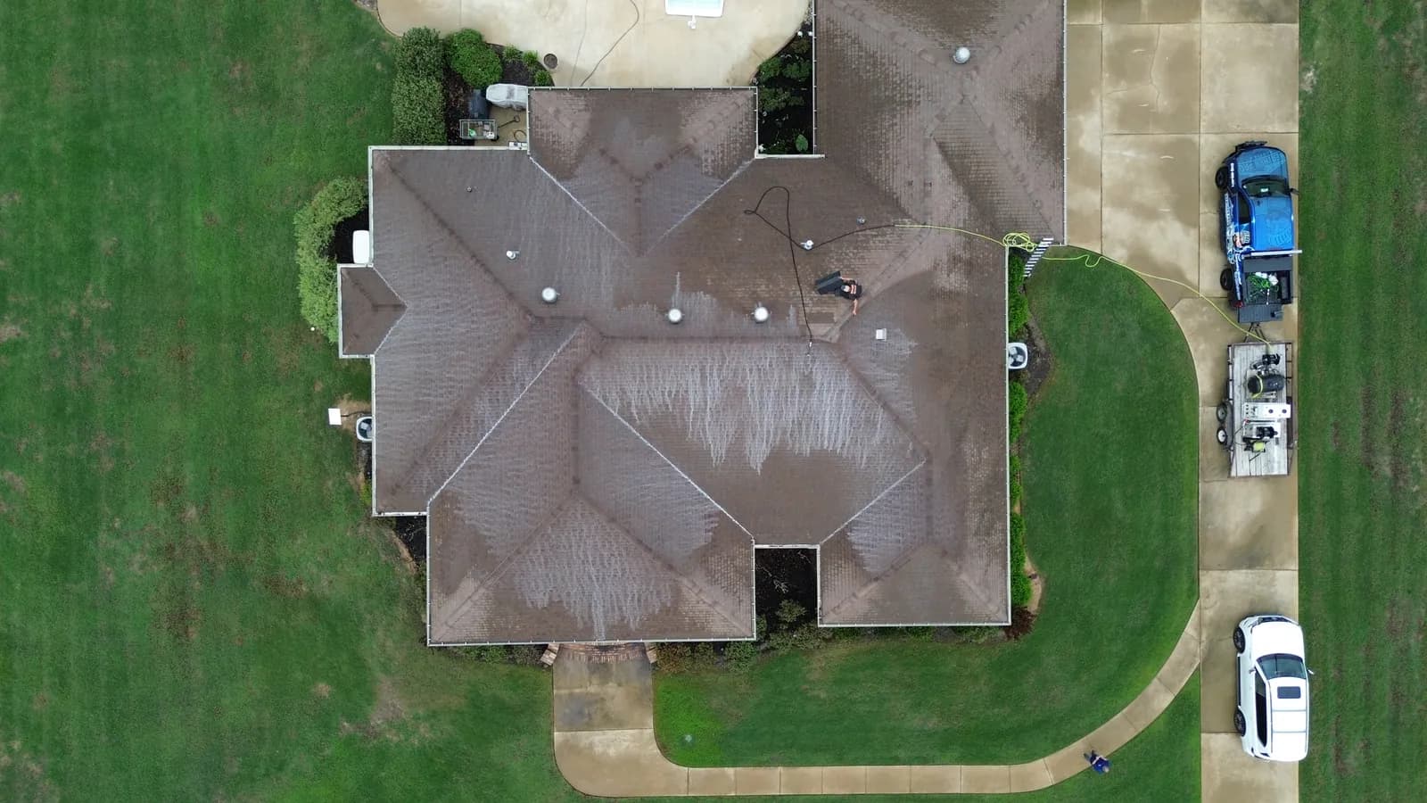 Overhead aerial of a hip-roof home being soft-washed, showing the chemistry pattern reaching every slope and valley