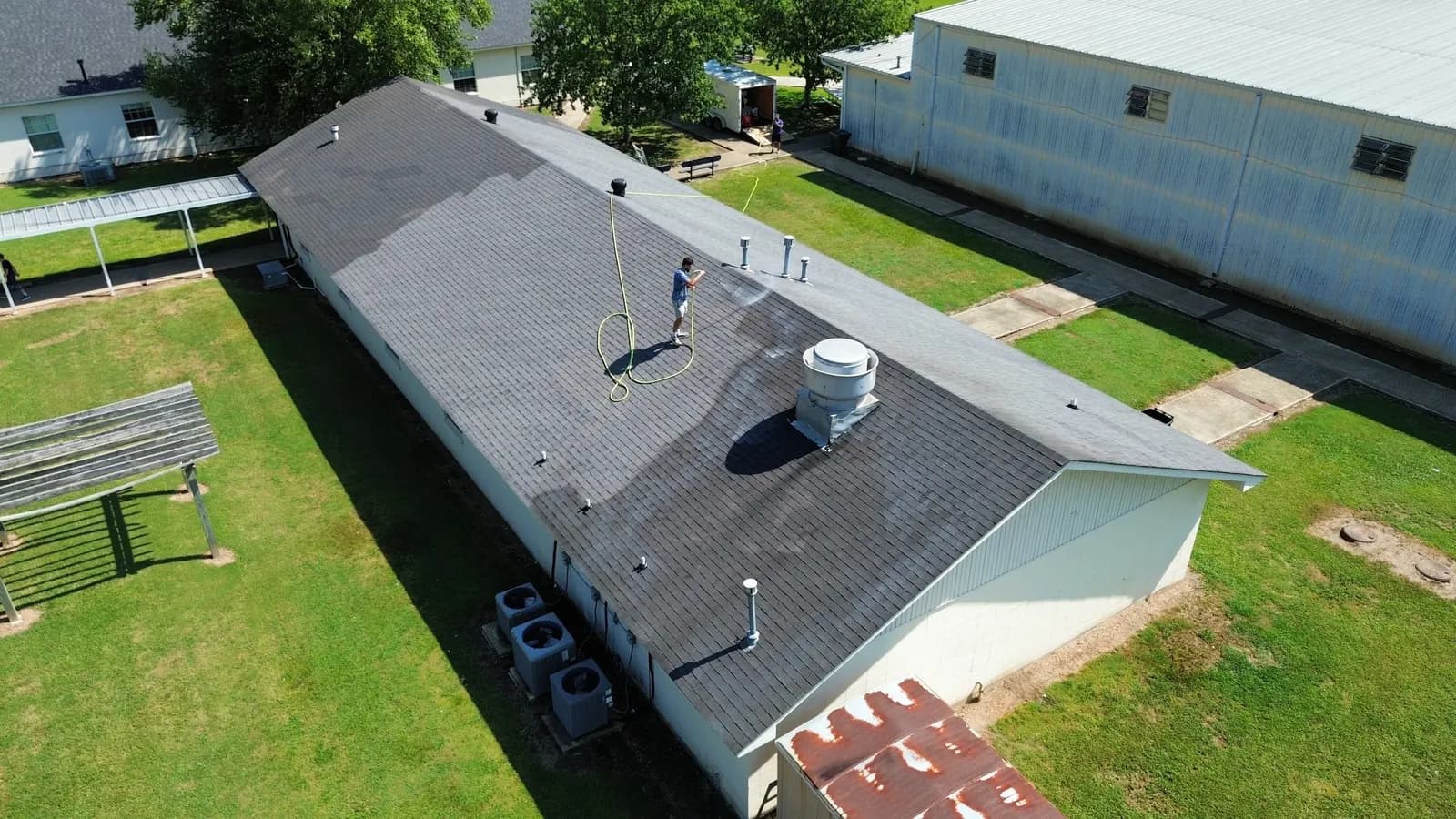 Long residential building mid-soft-wash, showing a clear color contrast between treated and untreated sections of the brown shingle roof