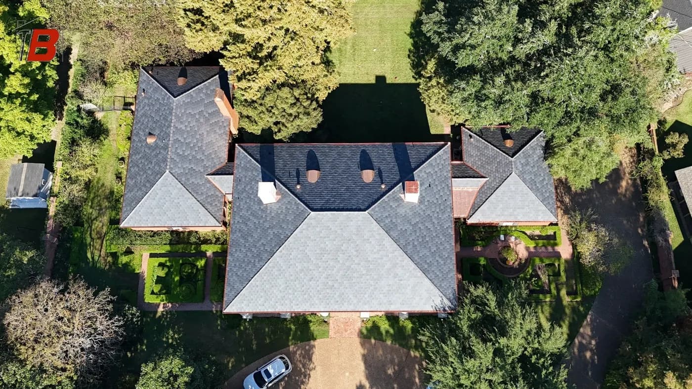 Drone aerial of a stately home with multiple gables and freshly installed light-gray architectural shingles