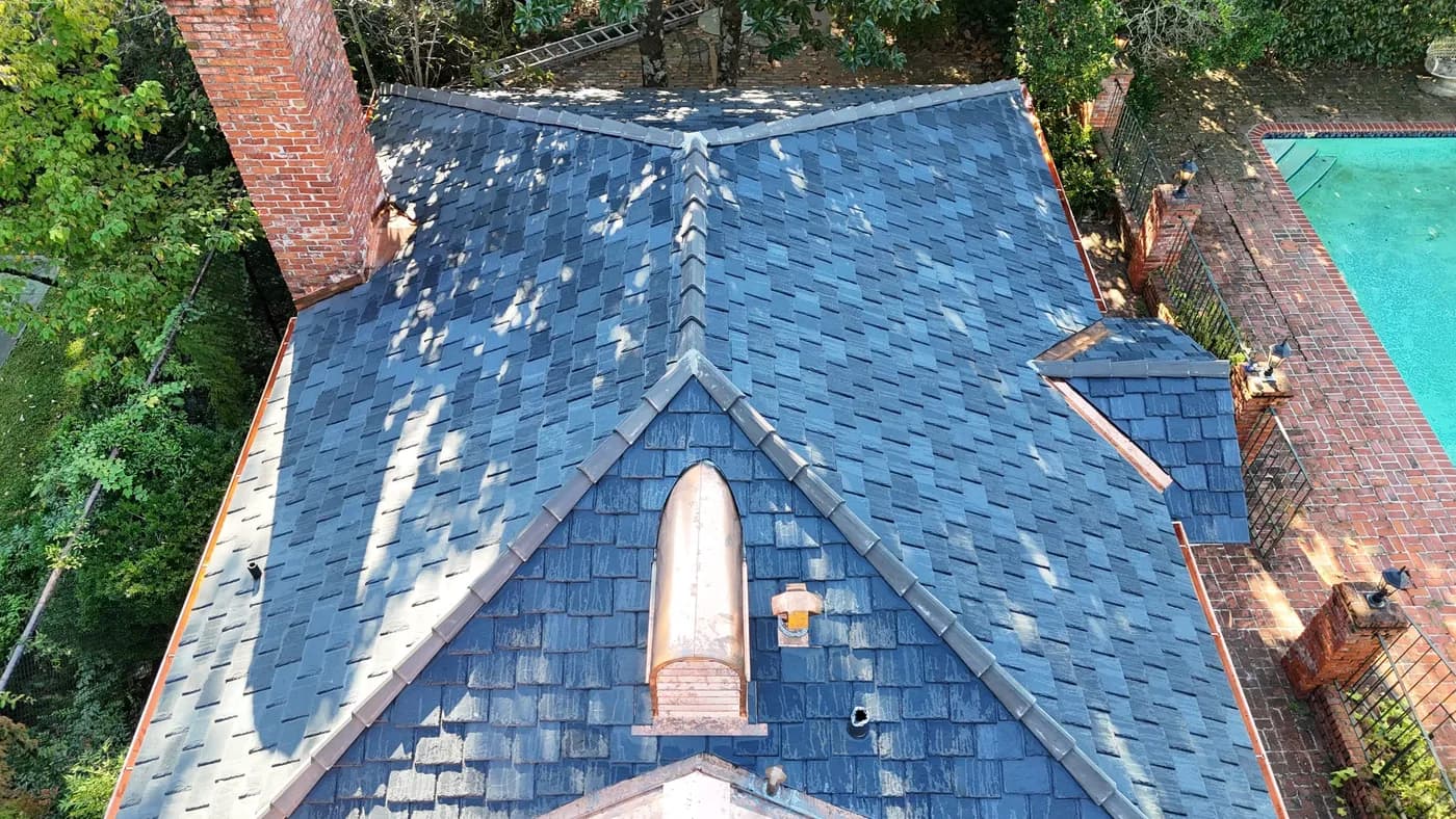 Aerial of a blue-gray slate roof with copper chimney cricket flashing detail