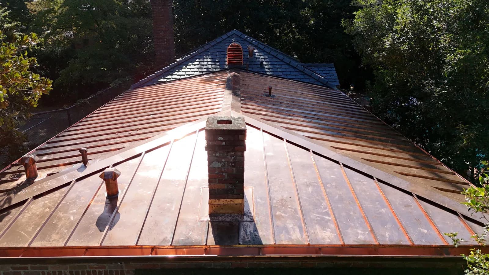 Copper standing-seam metal roof installed alongside a synthetic slate field