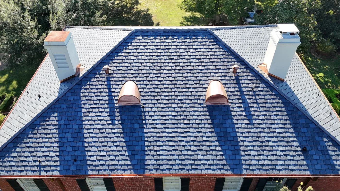 Drone aerial of a brick home's slate roof with two copper barrel-dormer caps