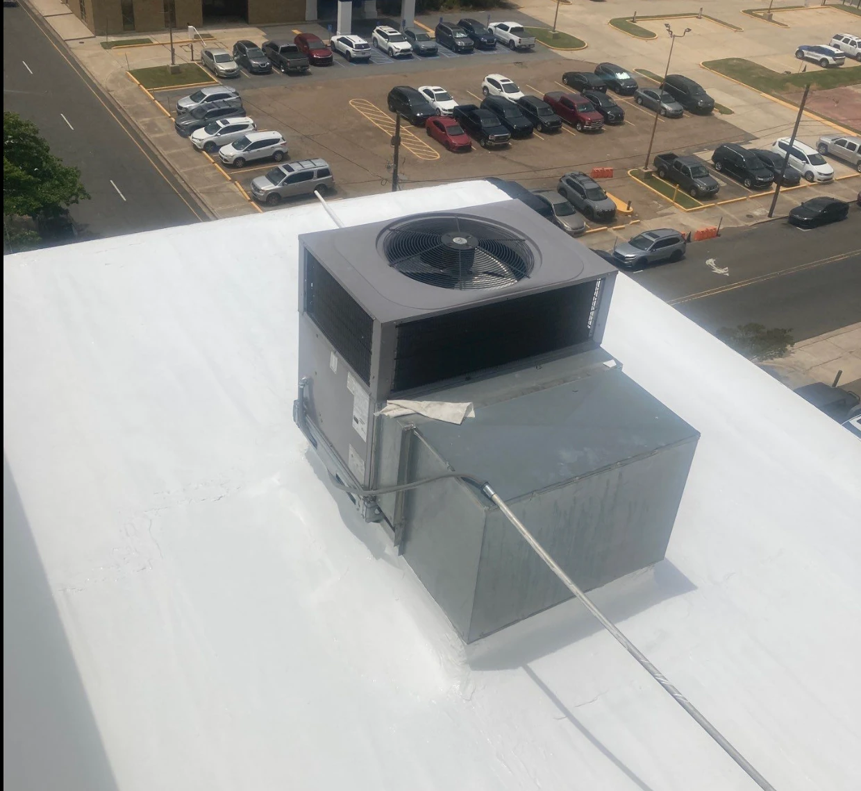 The same commercial flat roof after a bright white reflective roof coating was applied around the HVAC unit