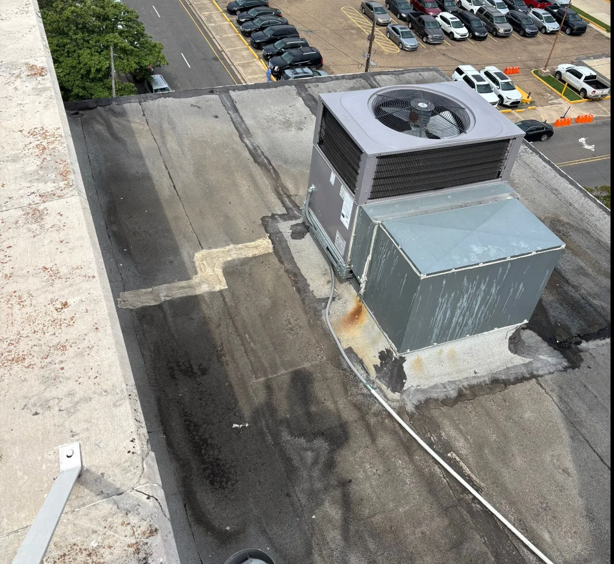 Aged dark modified bitumen commercial roof with patched repairs around a rooftop HVAC unit before coating