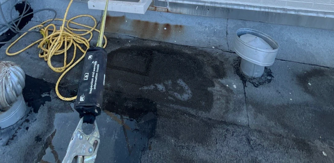 Dark ponding stain and standing water on a flat commercial roof next to a roof drain
