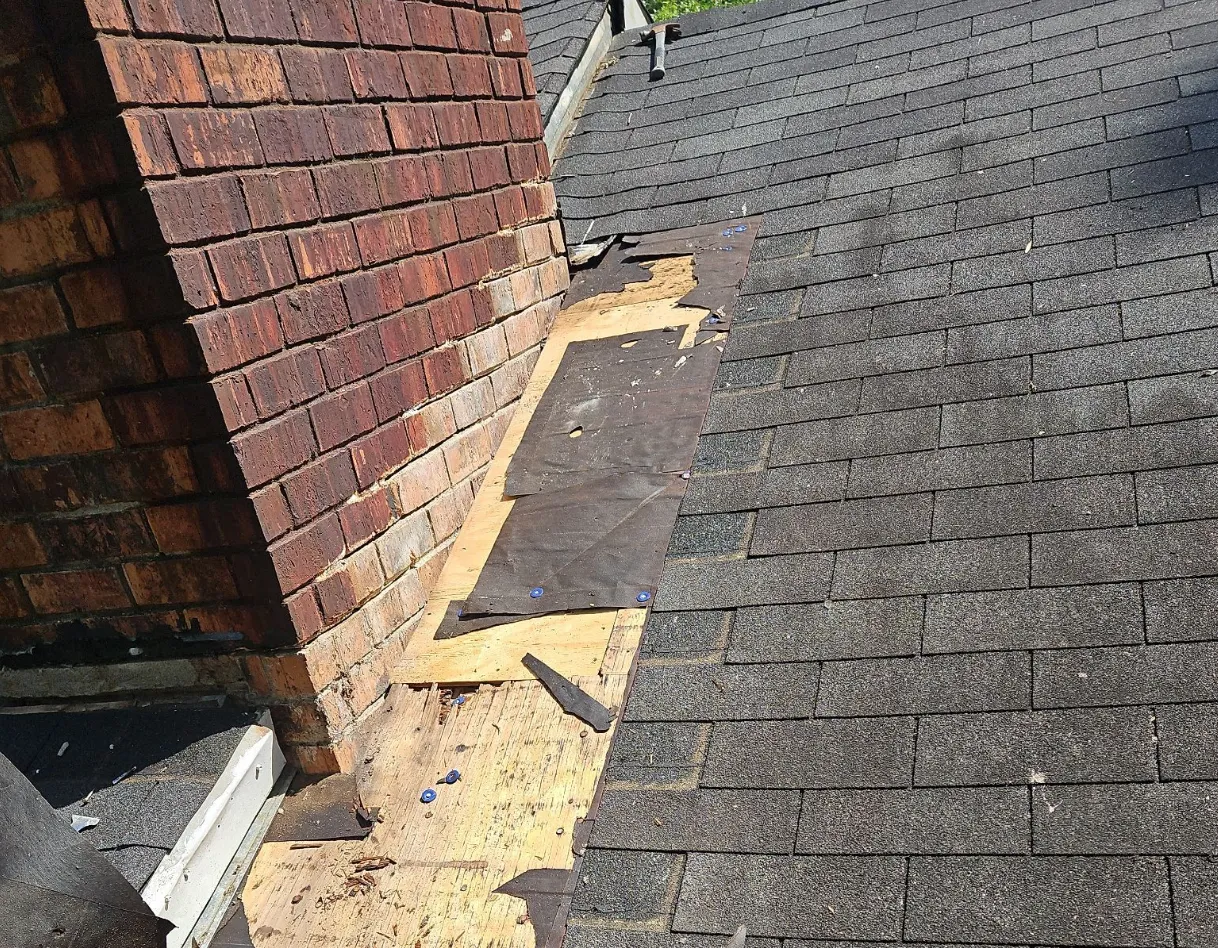 Chimney flashing opened up during an asphalt shingle roof repair, with new underlayment installed over the exposed decking