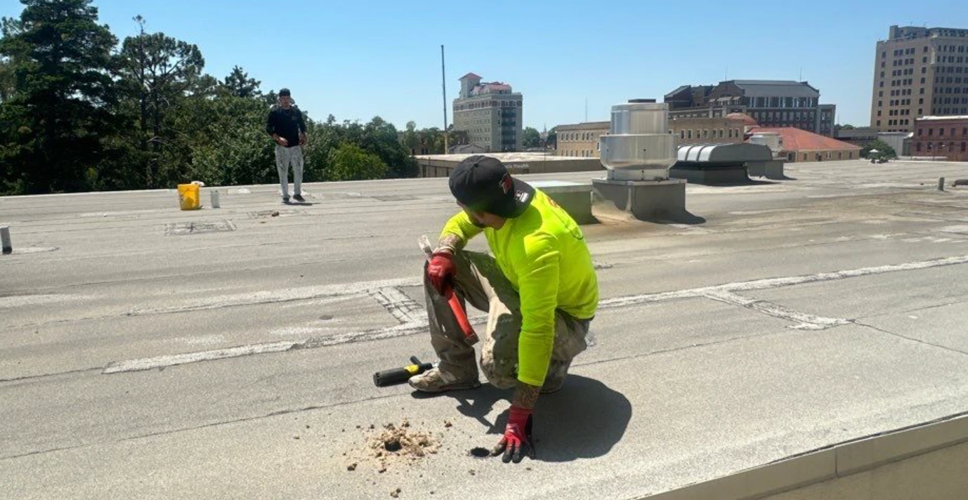 Roofing crew member performing a core-cut sample on a commercial flat roof