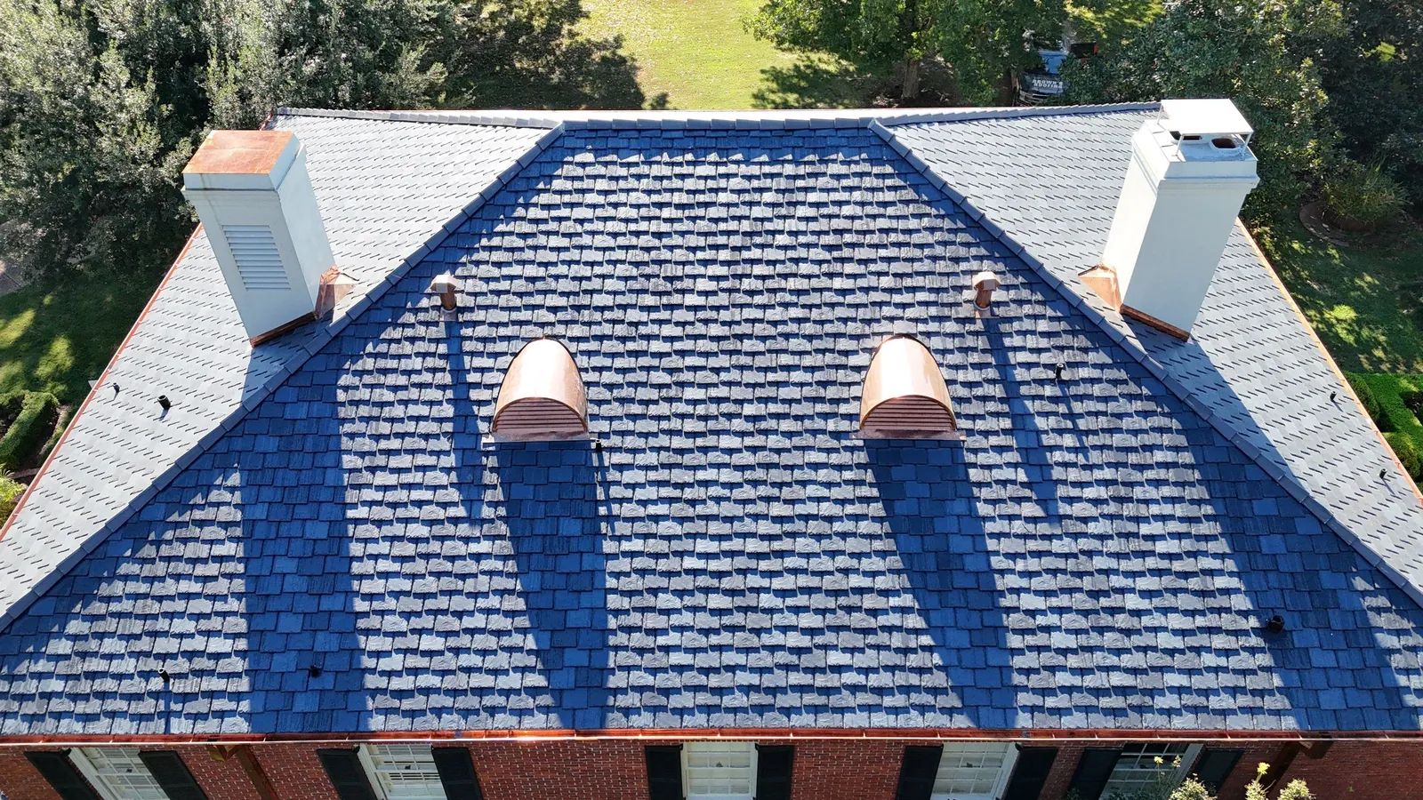 Aerial view of a synthetic slate roof with copper dormers and copper flashing at both chimneys