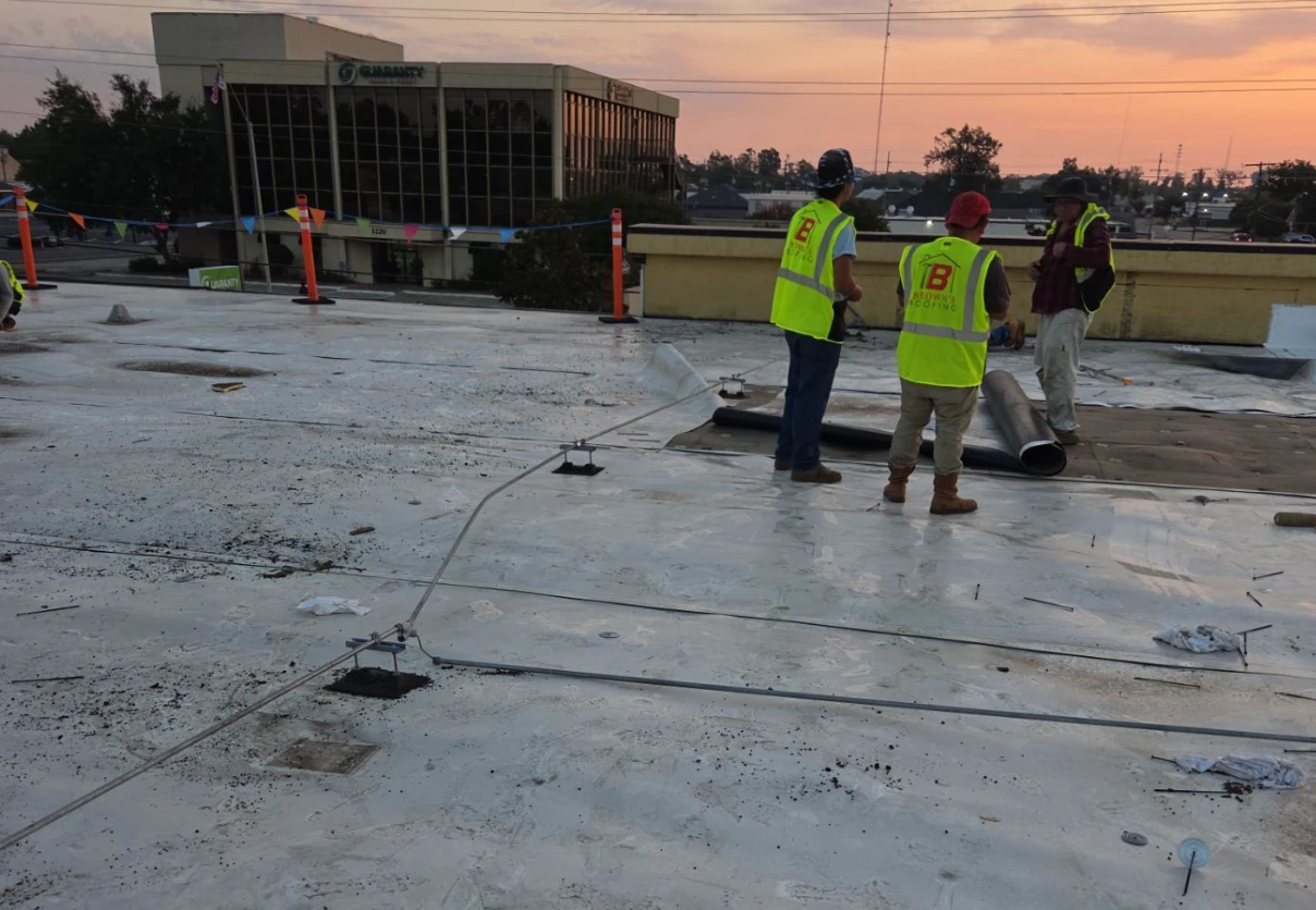 Brown's Roofing crew on the failing commercial roof in Monroe, LA at first light before tear-off begins