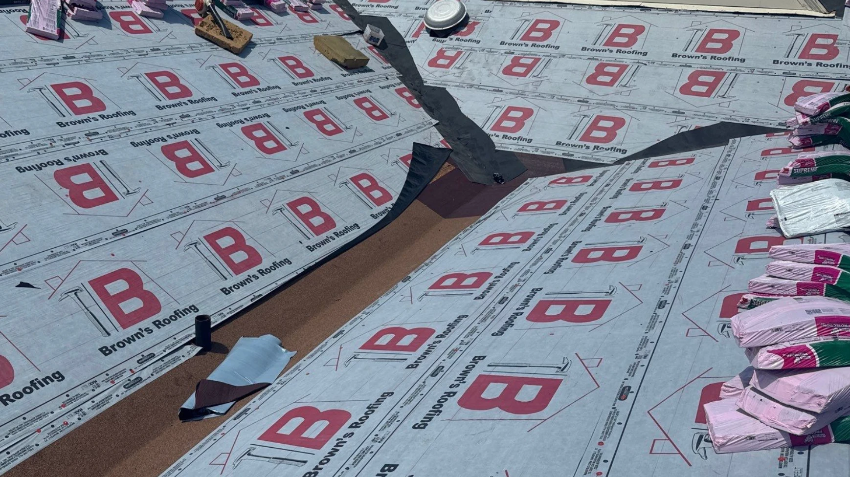 Modified bitumen membrane laid into a roof valley over synthetic underlayment, with Owens Corning Supreme shingle bundles staged across the deck