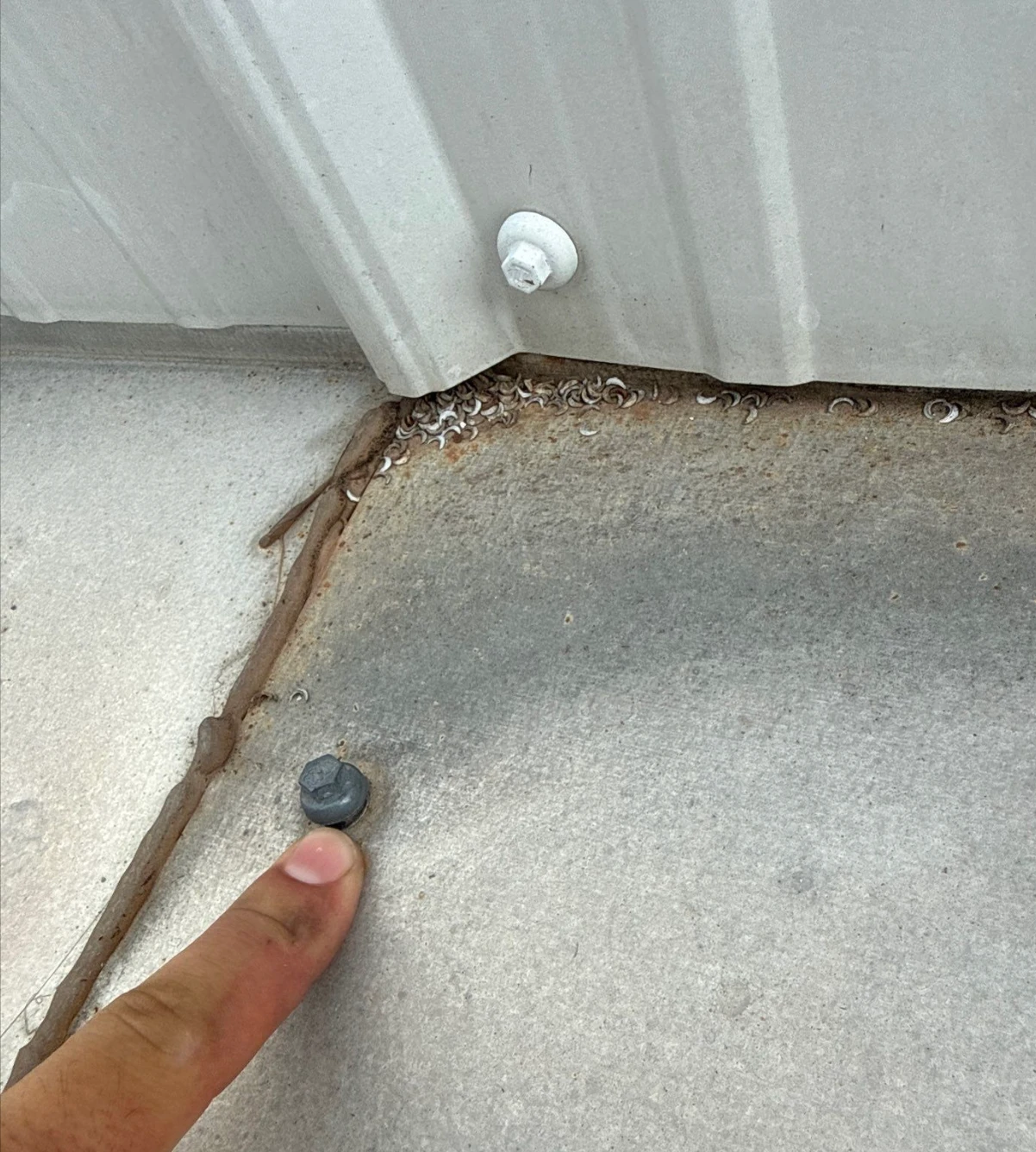 Metal shavings and a fastener at the base of a metal panel, pointed out during a roof overlay assessment