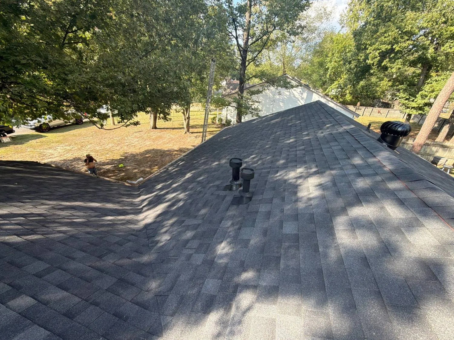 Completed asphalt shingle roof showing slopes meeting at a hip and a valley, with pipe boots and a turbine vent